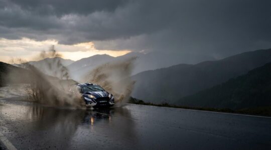 Vue cinématographique d'une voiture de rallye WRC projetant des gerbes d'eau sur route mouillée